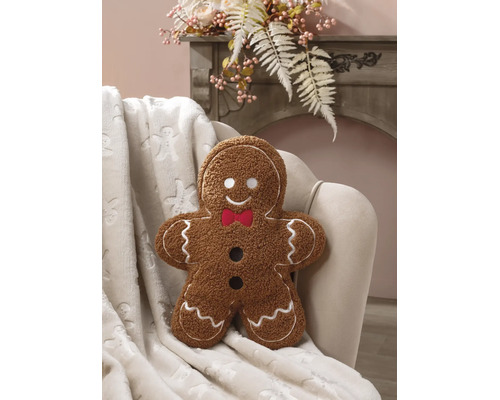 Prydnadskudde i form av en pepparkaksgubbe i teddy-plysch med vita broderier och röd fluga i en fåtölj.