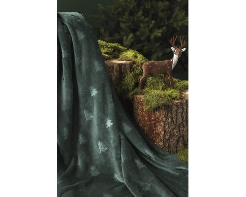 Mjuk mörkgrön filt med präglat mönster av granar, draperad bredvid en trädstubbe med mossa och en liten hjortfigur.