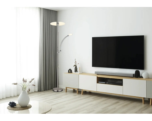 Modernt, ljust vardagsrum med en golvlampa i metall med läsarm bredvid en mediabänk med TV.