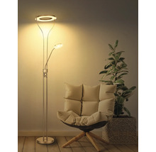 Modern golvlampa i metall med uplight och läsarm i ett vardagsrum bredvid en fåtölj och en växt. Varm belysning.