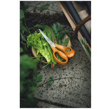 Fiskars örtsax ligger på nyskördade örter och sallad i en skål i trädgården på ett stengolv.