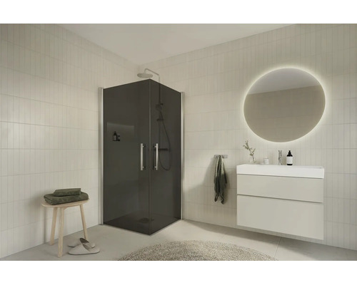 Modern badrumsmiljö med en hörndusch i gråtonat glas, vit kommod med LED-spegel och ljust kakel.
