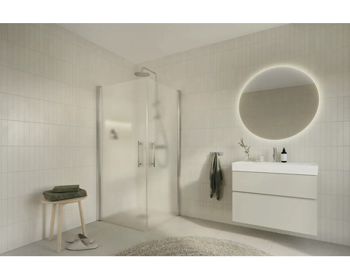 Modern, ljust badrum med hörn-duschkabin i glas, vit kommod, rund LED-spegel och beige kakel.
