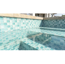 Pool med mosaikplattor på väggar och trappsteg, klart vatten och kantstenar.