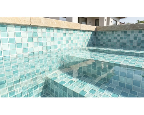 Pool med mosaikplattor på väggar och trappsteg, klart vatten och kantstenar.