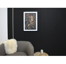 Modern väggdesign med svarta akustikpaneler av träribbor i ett organiserat vardagsrum med grå fåtölj och träbord.