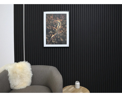 Modern väggdesign med svarta akustikpaneler av träribbor i ett organiserat vardagsrum med grå fåtölj och träbord.