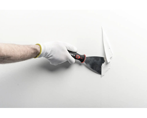 Hand med arbetshandske som använder en spackelspade för att ta bort tapet från en vägg.