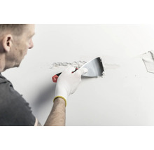 En person applicerar spackel på en vägg med en spackelspade av metall.
