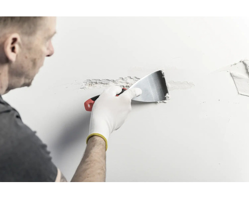 En person applicerar spackel på en vägg med en spackelspade av metall.