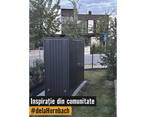 Modernt trädgårdsskjul i metall i mörkgrått på en gräsmatta i en trädgård framför ett hus.