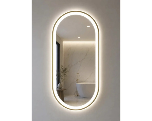 Oval badrumsspegel med guldram och LED-belysning. Spegeln reflekterar ett ljust badrum med fristående badkar och marmorvägg.