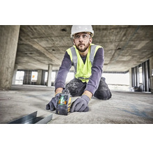 Hantverkare med skyddshjälm och reflexväst använder en Dewalt korslinjelaser på en betongbyggarbetsplats för exakt inriktning.