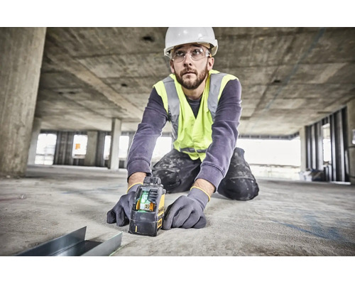 Hantverkare med skyddshjälm och reflexväst använder en Dewalt korslinjelaser på en betongbyggarbetsplats för exakt inriktning.