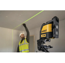 En byggarbetare i arbetskläder markerar en vägg med hjälp av en DeWalt korslaser på ett stativ inomhus.
