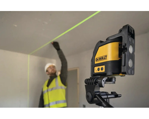 En byggarbetare i arbetskläder markerar en vägg med hjälp av en DeWalt korslaser på ett stativ inomhus.