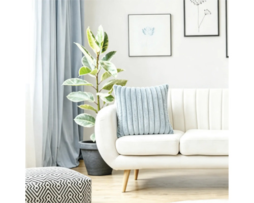 En mjuk räfflad kudde på en ljus soffa i ett ljust vardagsrum med en växt och en geometrisk sittpuff.