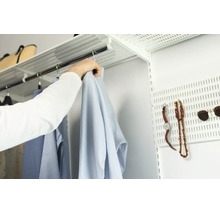 Ett öppet hyllsystem med klädstång och en perforerad platta för organisering av kläder och accessoarer i en klädkammare.