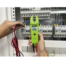 En KPS tångamperemeter hålls i handen för att mäta spänningen i en elcentral med installerade dvärgbrytare.
