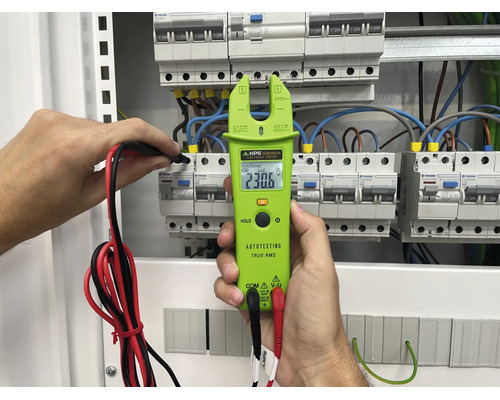 En KPS tångamperemeter hålls i handen för att mäta spänningen i en elcentral med installerade dvärgbrytare.