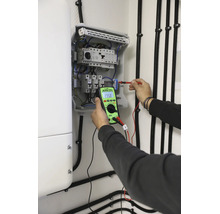 Elektriker mäter spänning i en öppen säkringslåda med en digital KPS-multimeter för elektrisk feldiagnostik.