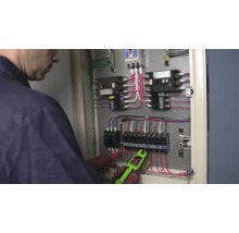 Elektriker mäter spänning i ett öppet elskåp med en digital strömmätare.