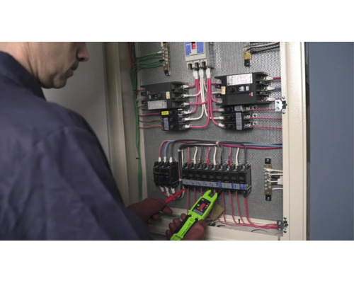 Elektriker mäter spänning i ett öppet elskåp med en digital strömmätare.
