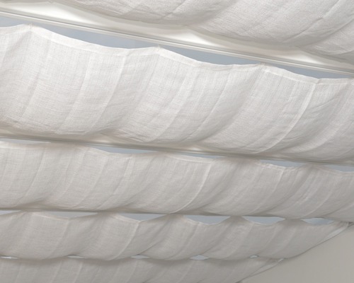Detaljbild av veckade, vita tygstycken under ett tak, del av en textil rumsdesign
