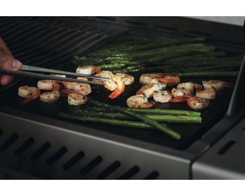 Grillade räkor och sparris vänds med en grilltång.