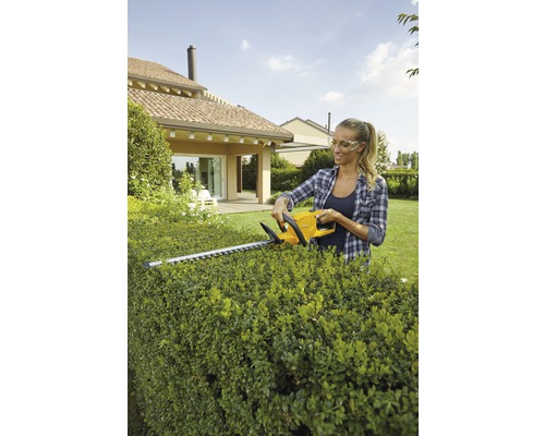 Kvinna klipper häck med en häcksax i trädgården.