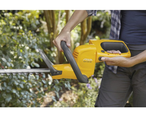 Person håller en gul Stiga häcksax SHT 100 AE.