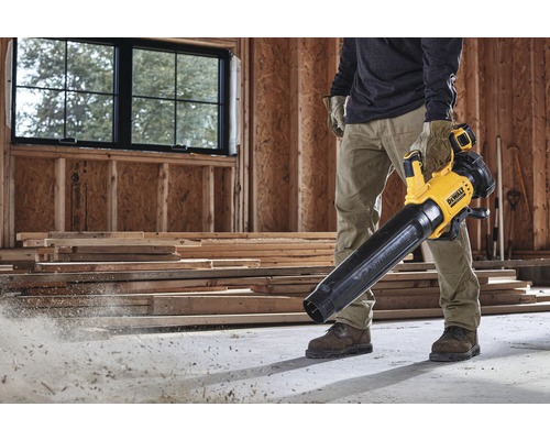 En man använder en gul och svart DeWalt sladdlös lövblås på en byggarbetsplats.