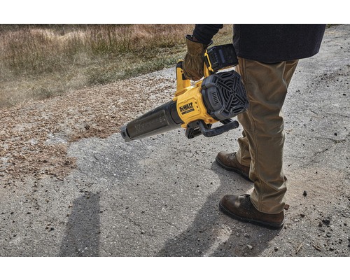 En person använder en gul sladdlös lövblås från DeWalt på en obelagd yta.