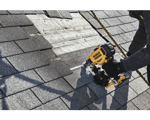 En arbetare fäster takspån med en DeWalt pneumatisk häftpistol på ett tak.