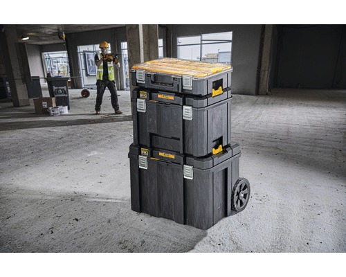 Staplingsbara verktygslådor med hjul och byggnadsarbetare i bakgrunden