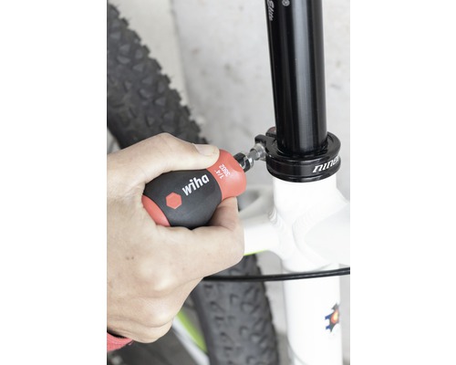 En person fäster en cykelsadelstolpe med en Wiha-skruvmejsel.