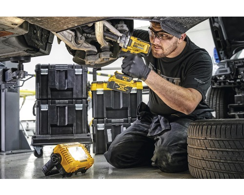 Mekaniker som arbetar med en sladdlös mutterdragare på en bil, med verktygslådor och en arbetslampa i bakgrunden.