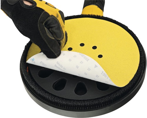 En hand med skyddshandske fäster sandpapper på en slipplatta.