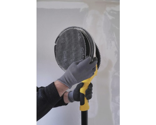 En person använder en gipsskiveslipmaskin på en vägg.