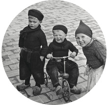 Historiskt foto av tre barn i traditionella kläder, en på en trehjuling