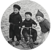 Tre barn i traditionella kläder, en på en trehjuling