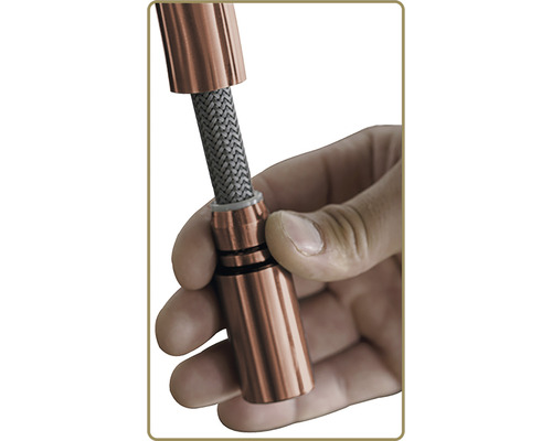 En hand håller en kopparfärgad krananslutning med en grå flätad ledning.