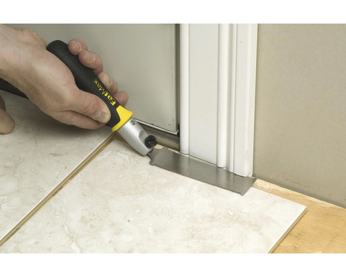 En person sågar en dörrkarm på ett klinkergolv med en handsåg.