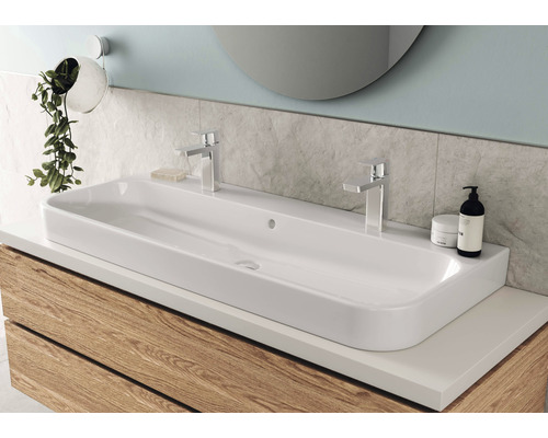 Tvättställ i badrum med två kranar, monterat på ett underskåp med träfront