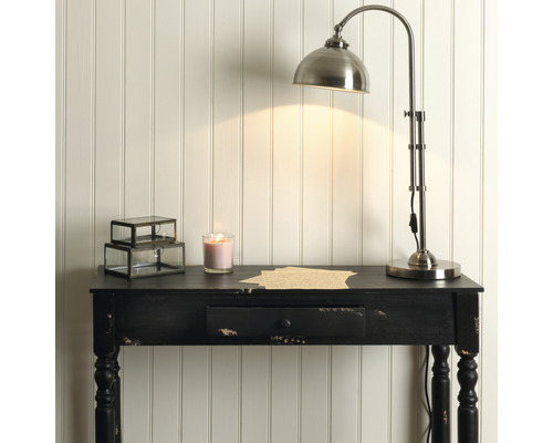 Miljöbild med en skrivbordslampa, ett ljus, en låda och ett svart bord framför en väggpanel.