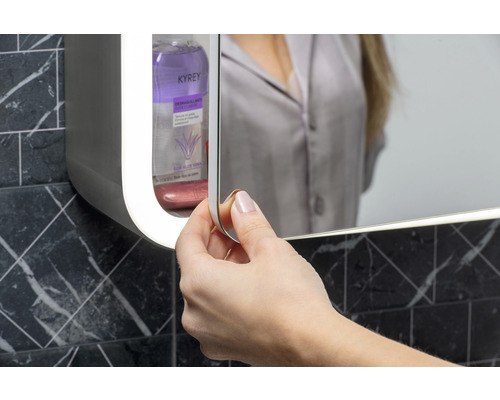 Kvinna öppnar spegelskåp i badrummet