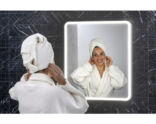 Kvinna med handduk på huvudet framför en upplyst badrumsspegel