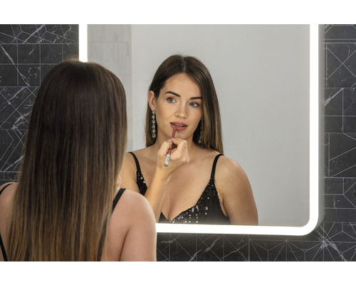 Kvinna applicerar läppstift framför en upplyst spegel i badrummet