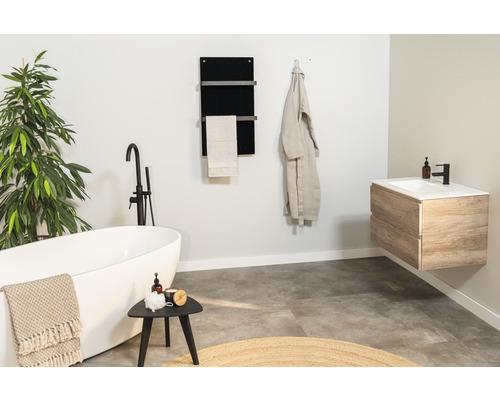 Ljust badrum med badkar, tvättställ, handdukstork och växt för en trevlig atmosfär.