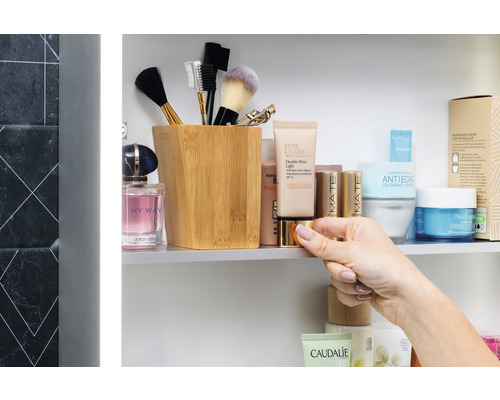 Badrumsscen med kosmetiska produkter, sminkborstar i en behållare och en hand som håller en burk.